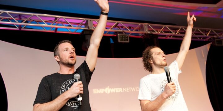 Two speakers with arms raised rallying the crowd from stage at Empower Network's 2012 Atlanta event