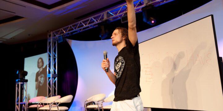 Trainer pointing skyward beside a whiteboard reading Be Do Have during a teaching session at Empower Network's 2012 Atlanta event
