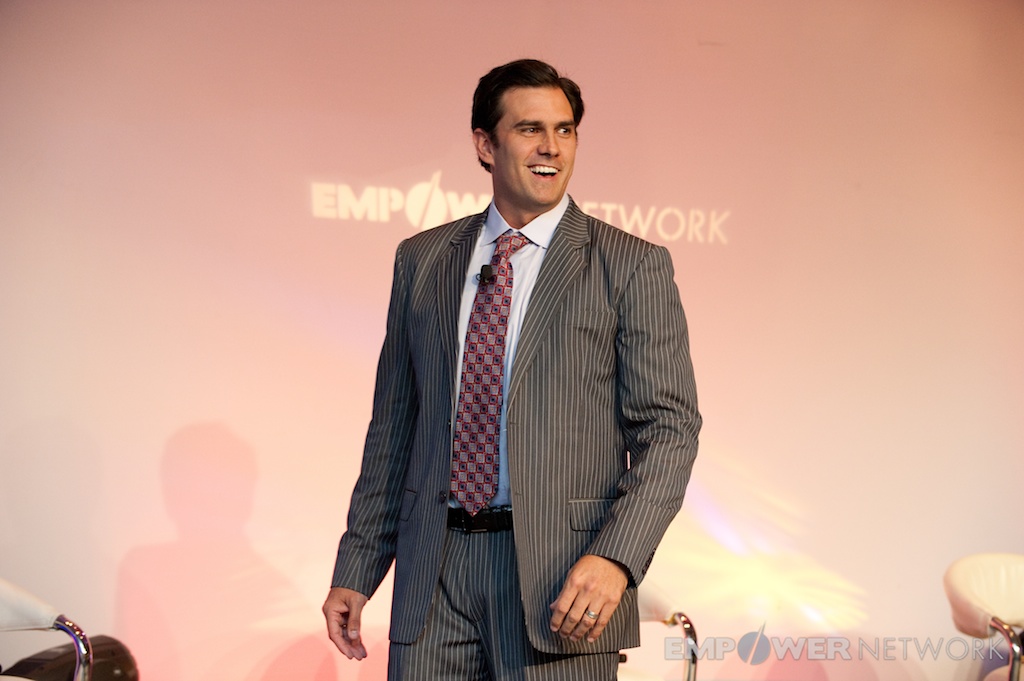 Speaker in a pinstripe suit smiling on stage in front of the Empower Network backdrop at the 2012 Atlanta event