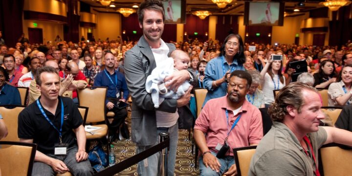 Smiling attendee cradling a baby while standing in a packed audience at Empower Network's 2012 Atlanta event