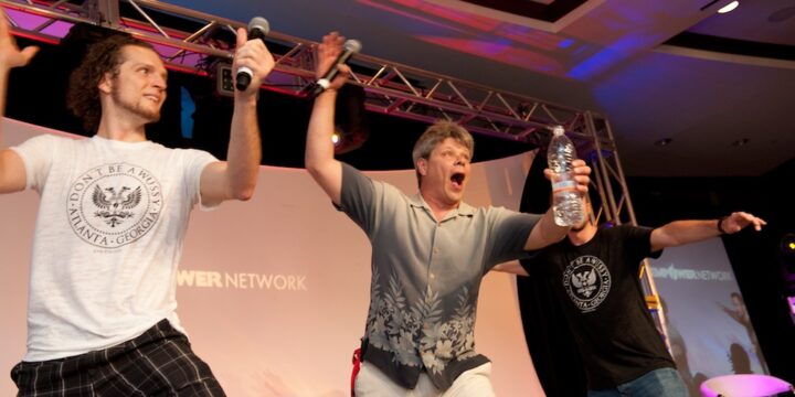 Three presenters clowning around with arms outstretched on stage at Empower Network's 2012 Atlanta event