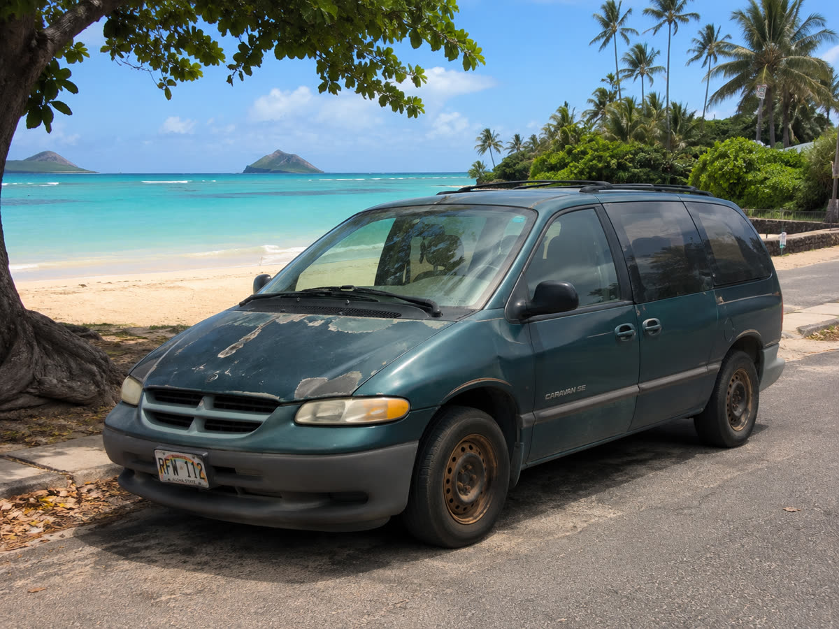 A weathered 1996 Dodge Caravan parked by the beach in Hawaii